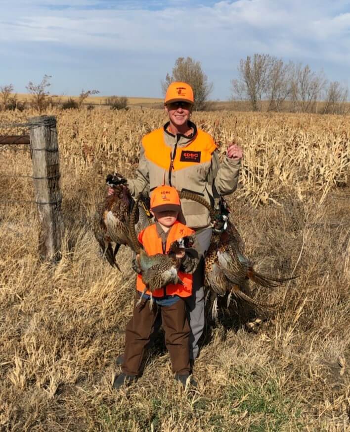 a woman and a boy holding hunted pheasants