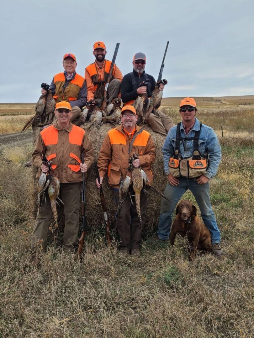 a group of men and a dog with their hunted pheasants