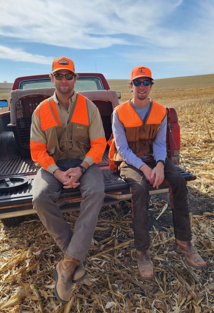 two people wearing hats sitting at the back side of a car